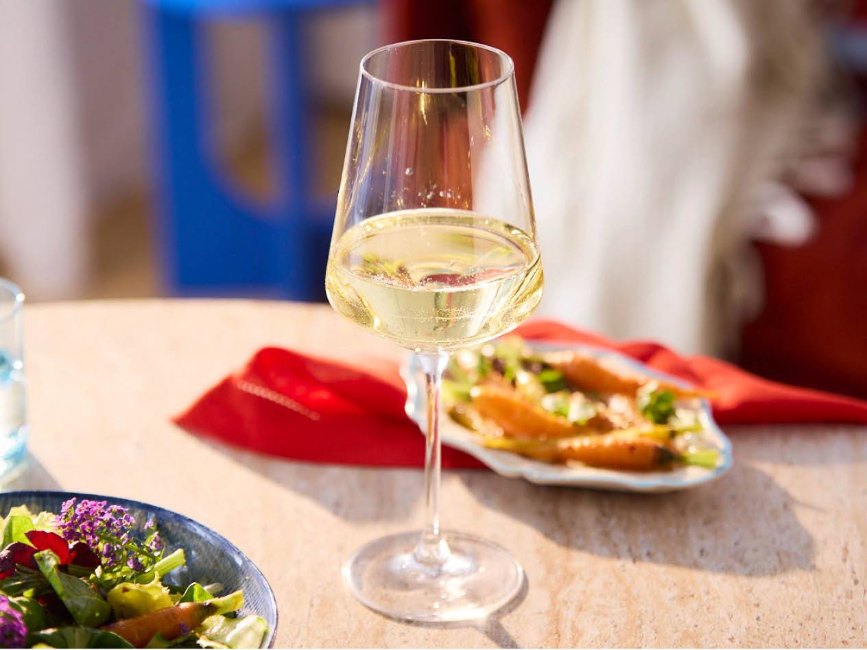 Ein Glas Weißwein steht auf einem Tisch neben einem Teller mit Salat.