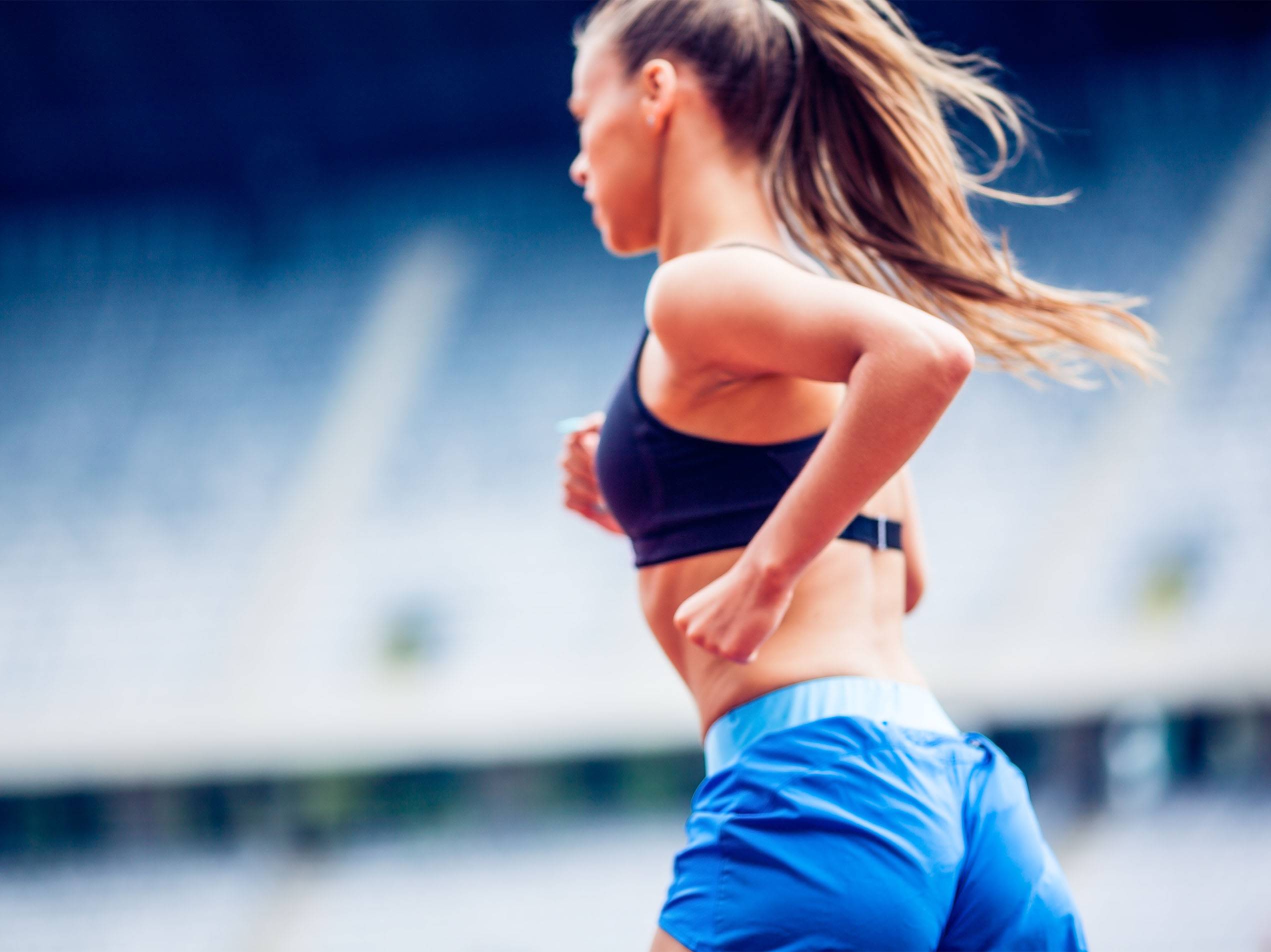Eine Frau in Sportkleidung läuft auf einer blauen Laufbahn.