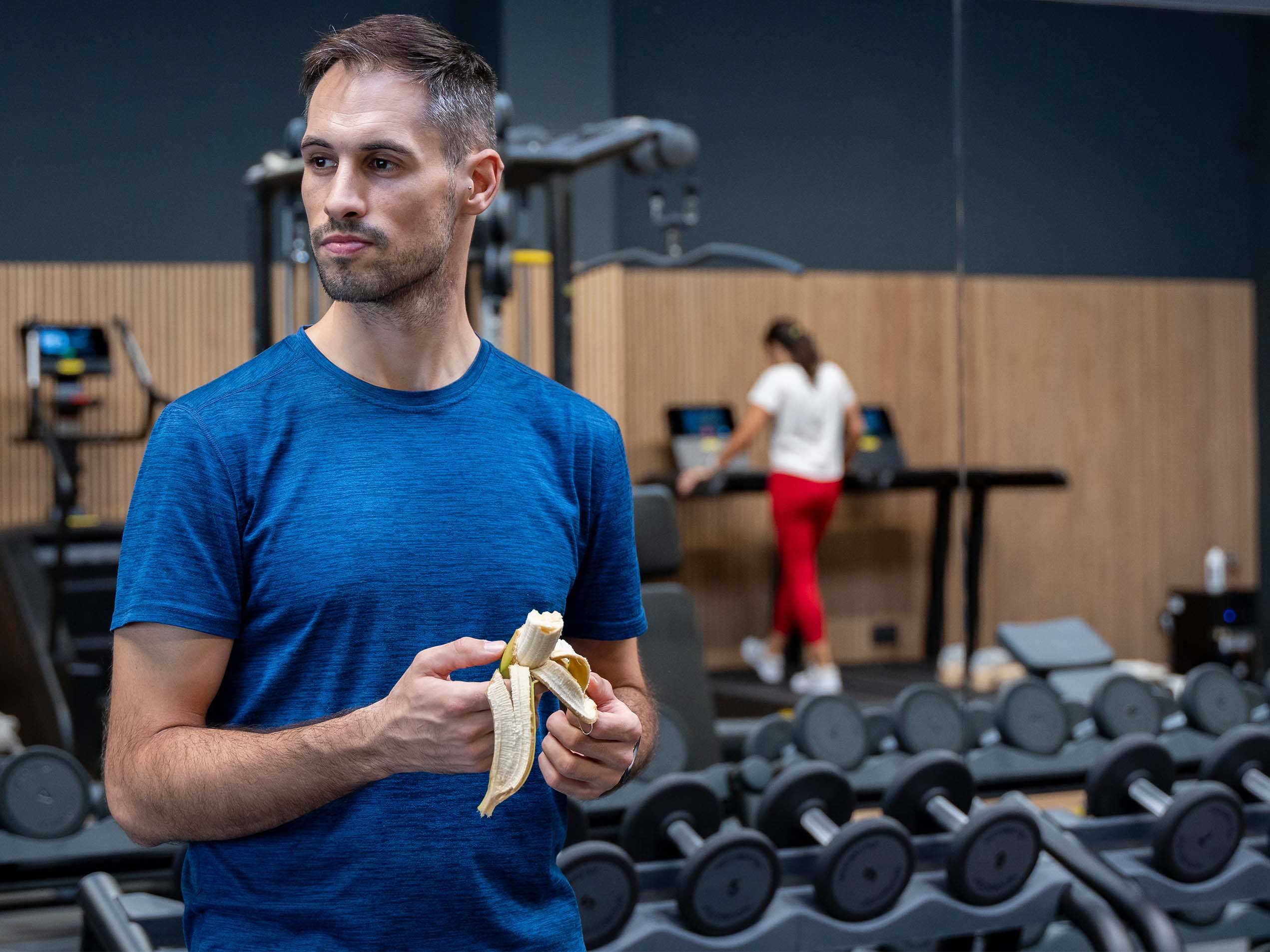 Mann isst Banane im Fitnessstudio mit Hanteln und Laufbändern.
