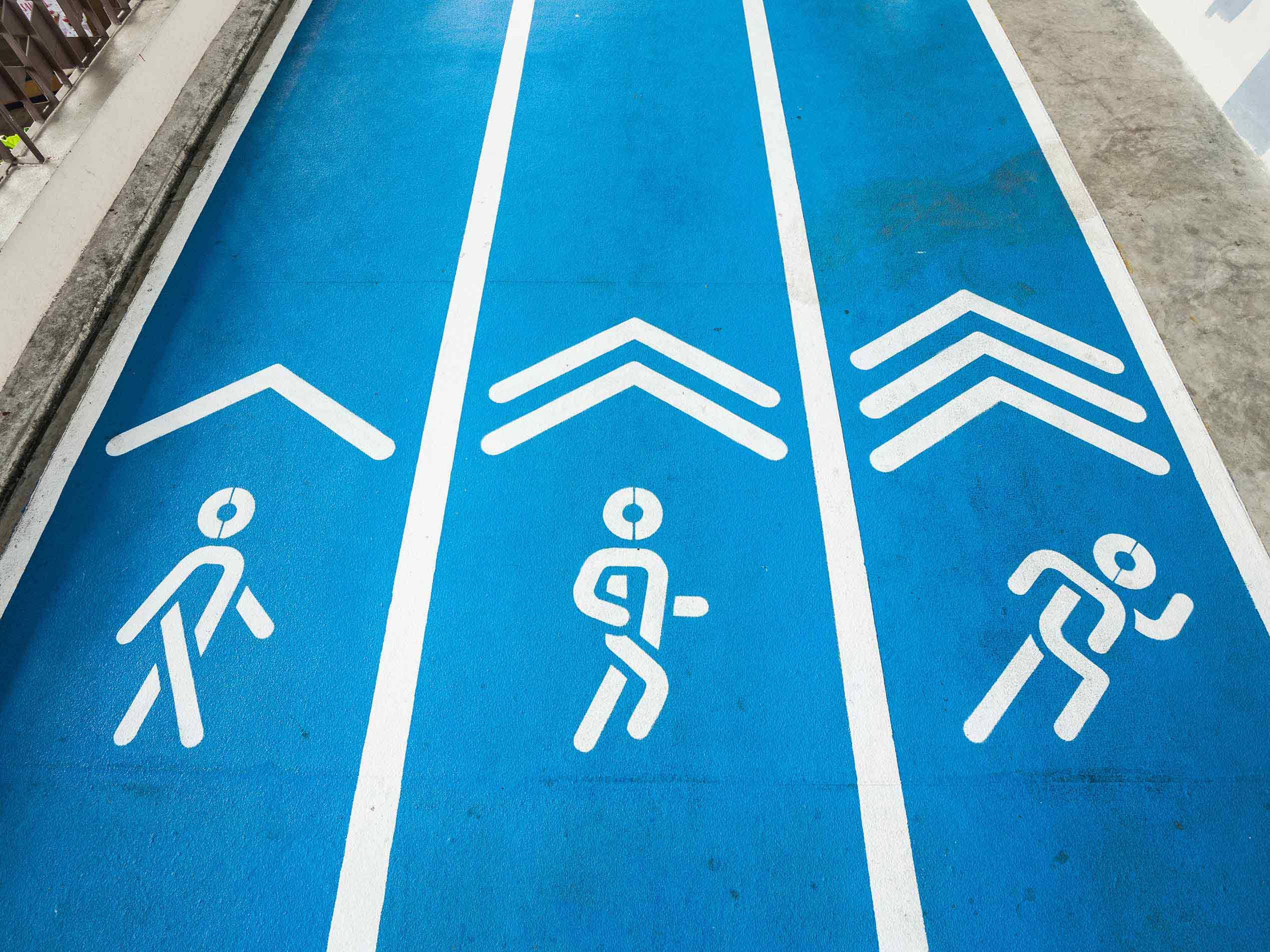 Blauer Gehweg mit Piktogrammen, die Gehen, Joggen und Laufen darstellen.