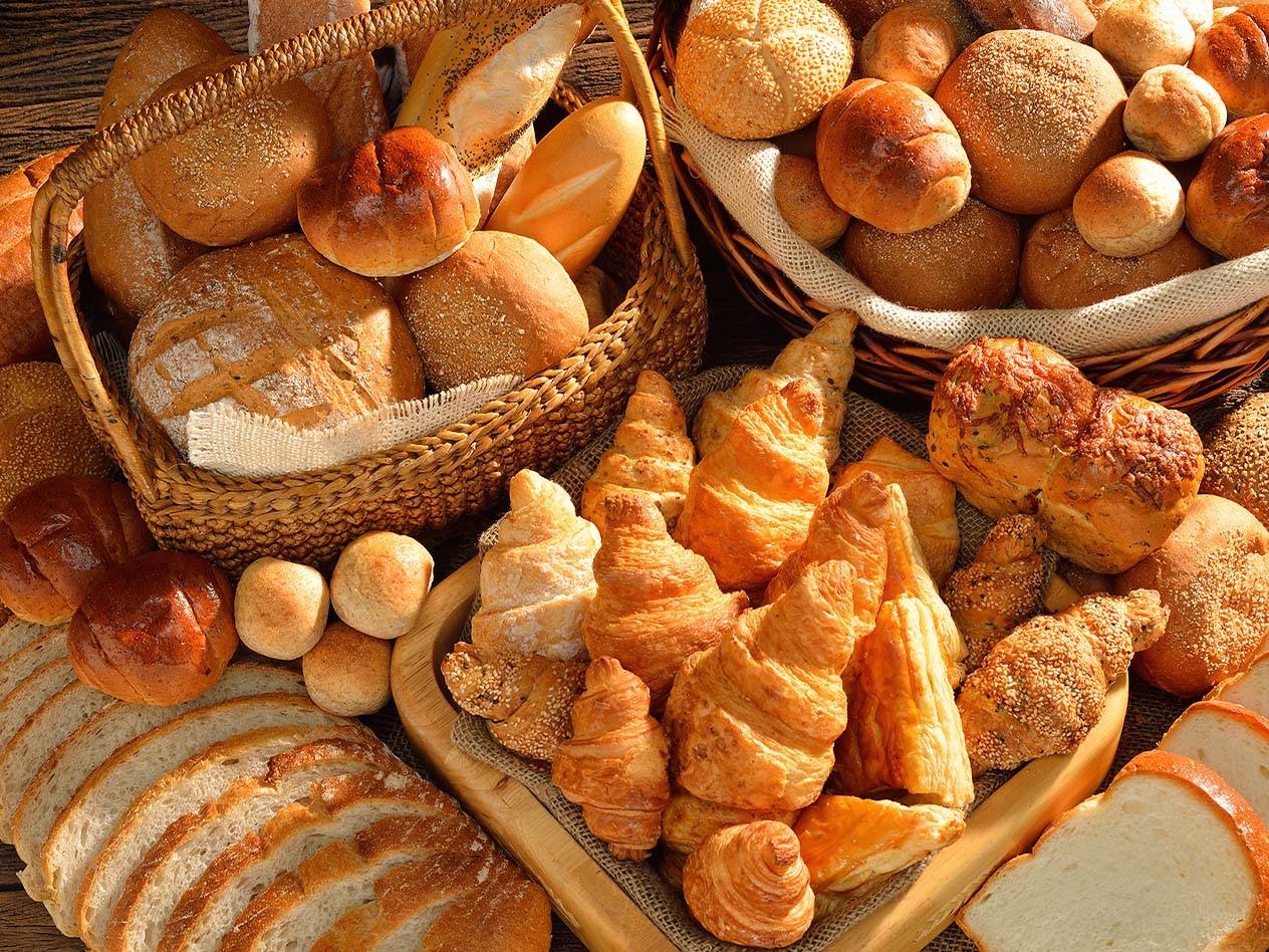 Eine große Auswahl an Brot, Brötchen und Croissants in Körben und auf einem Holzbrett.