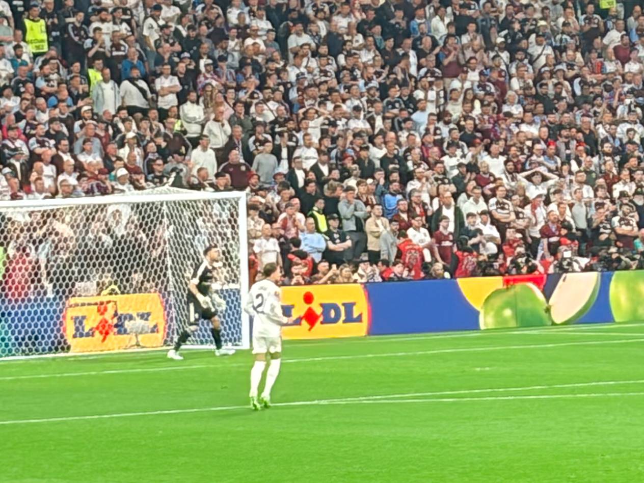 Fußballstadion mit Zuschauern, Spieler auf dem Feld und Bandenwerbung mit Obst.
