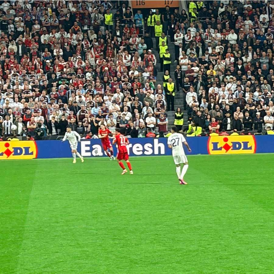 Fußballspieler auf dem Feld mit Zuschauern im Hintergrund und Werbebanden für frische Lebensmittel.