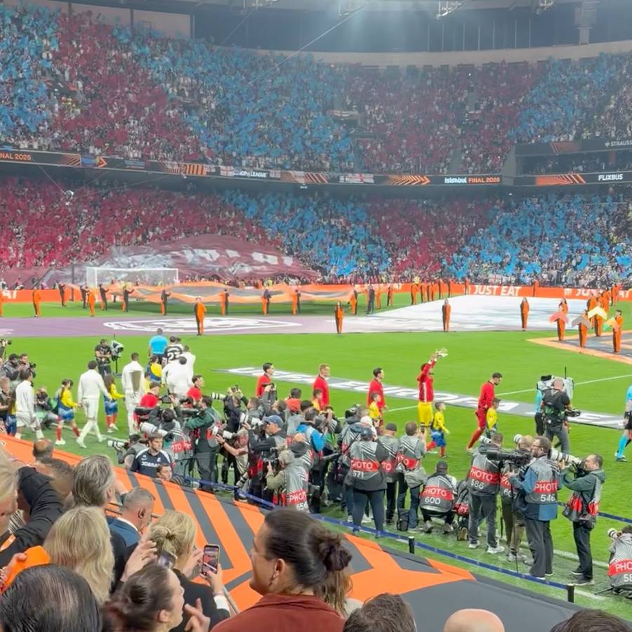 Ein Fußballstadion mit rot und blau gekleideten Fans, Spielern und Fotografen auf dem Feld.