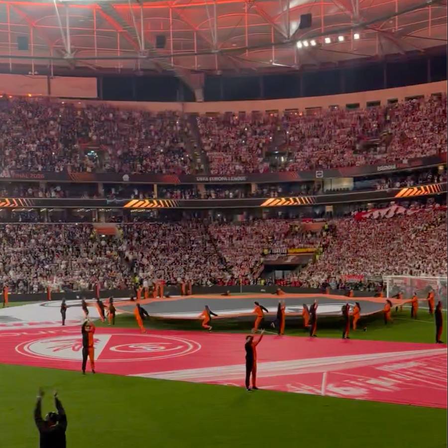 Ein Stadion voller Fans, während eine große rote Plane auf dem Spielfeld ausgebreitet wird.