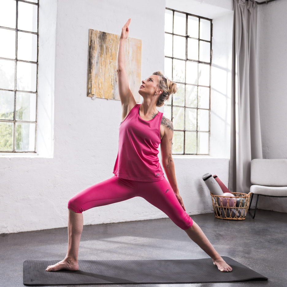Frau macht Yoga in pinker Sportkleidung in einem hellen Raum.
