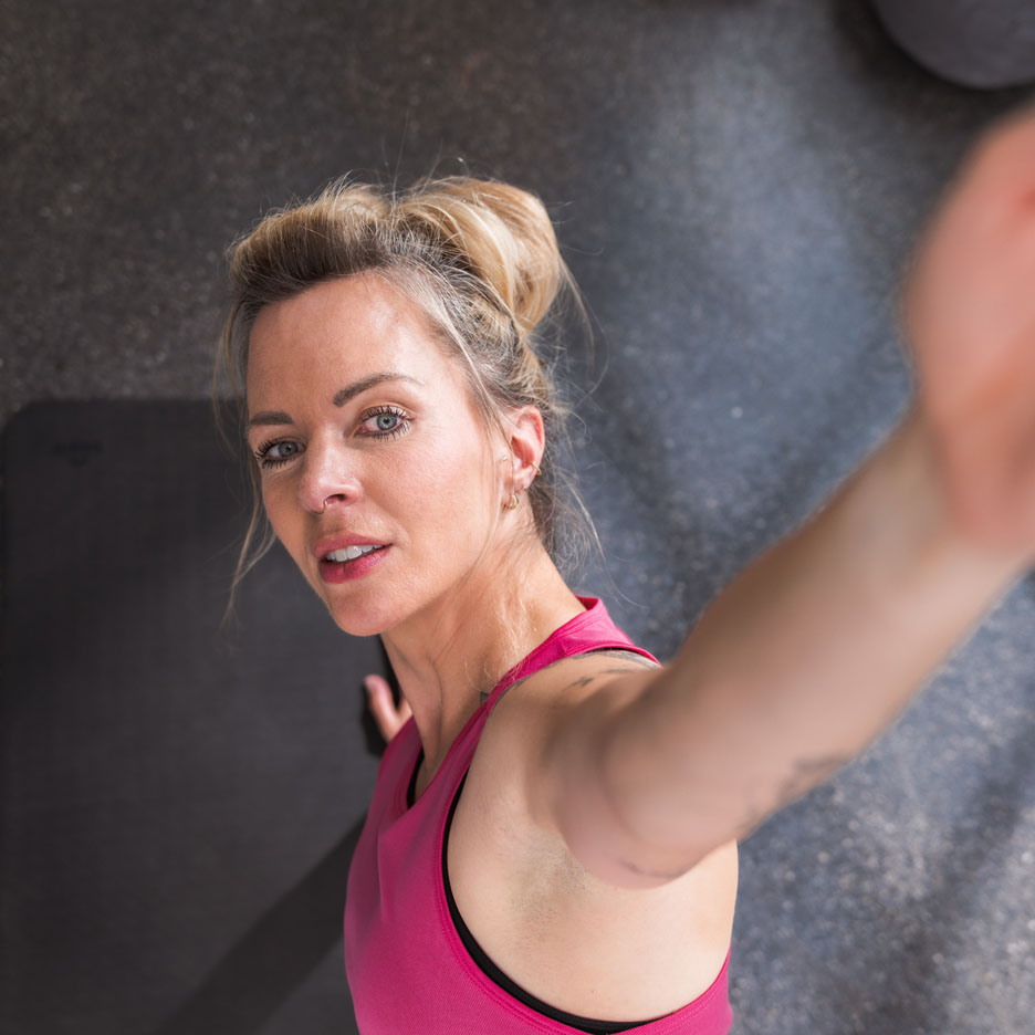 Eine Frau in einem pinken Sporttop macht ein Selfie im Fitnessstudio.