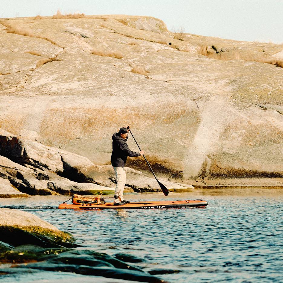 Mann paddelt auf einem orangefarbenen Stand-Up-Paddleboard auf einem felsigen See.