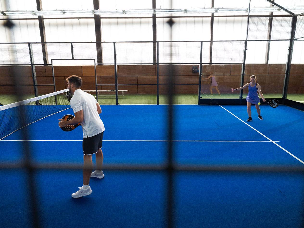 Zwei Personen spielen Padel auf einem blauen Platz, der Mann hält einen Schläger.