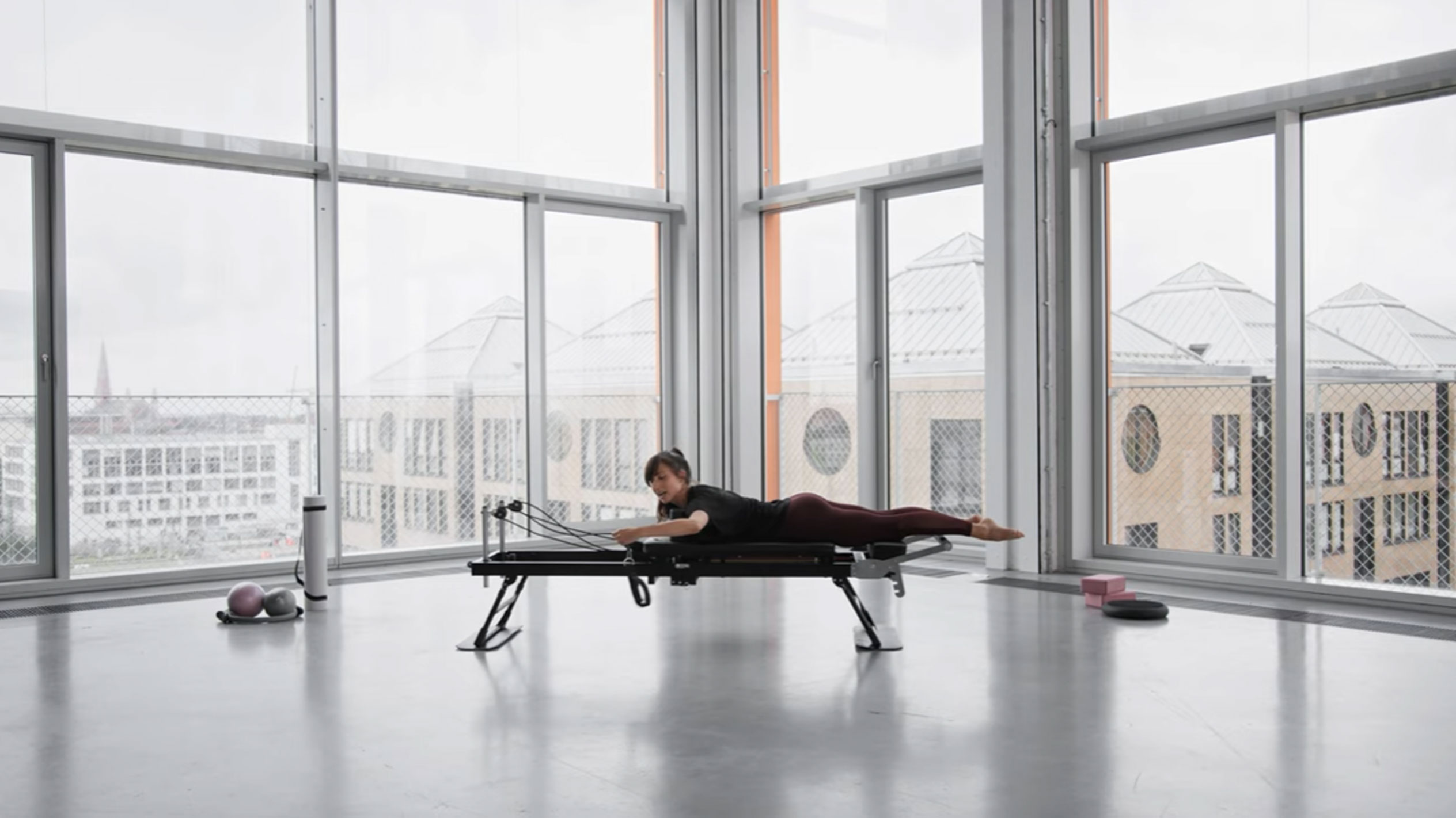 Frau macht Pilates auf einem Reformer, mit Blick auf die Stadt.