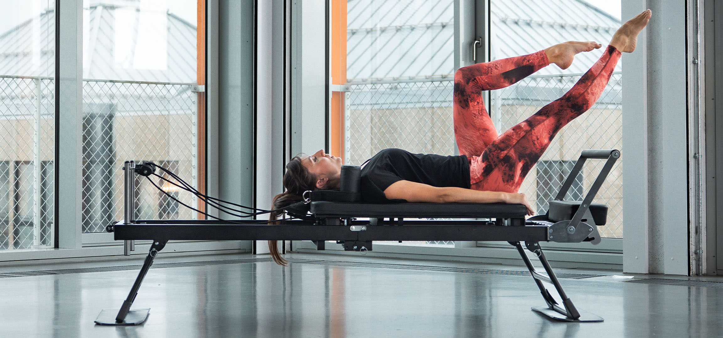 Frau macht Pilates auf einem Reformer, mit Fitnesszubehör in der Nähe.
