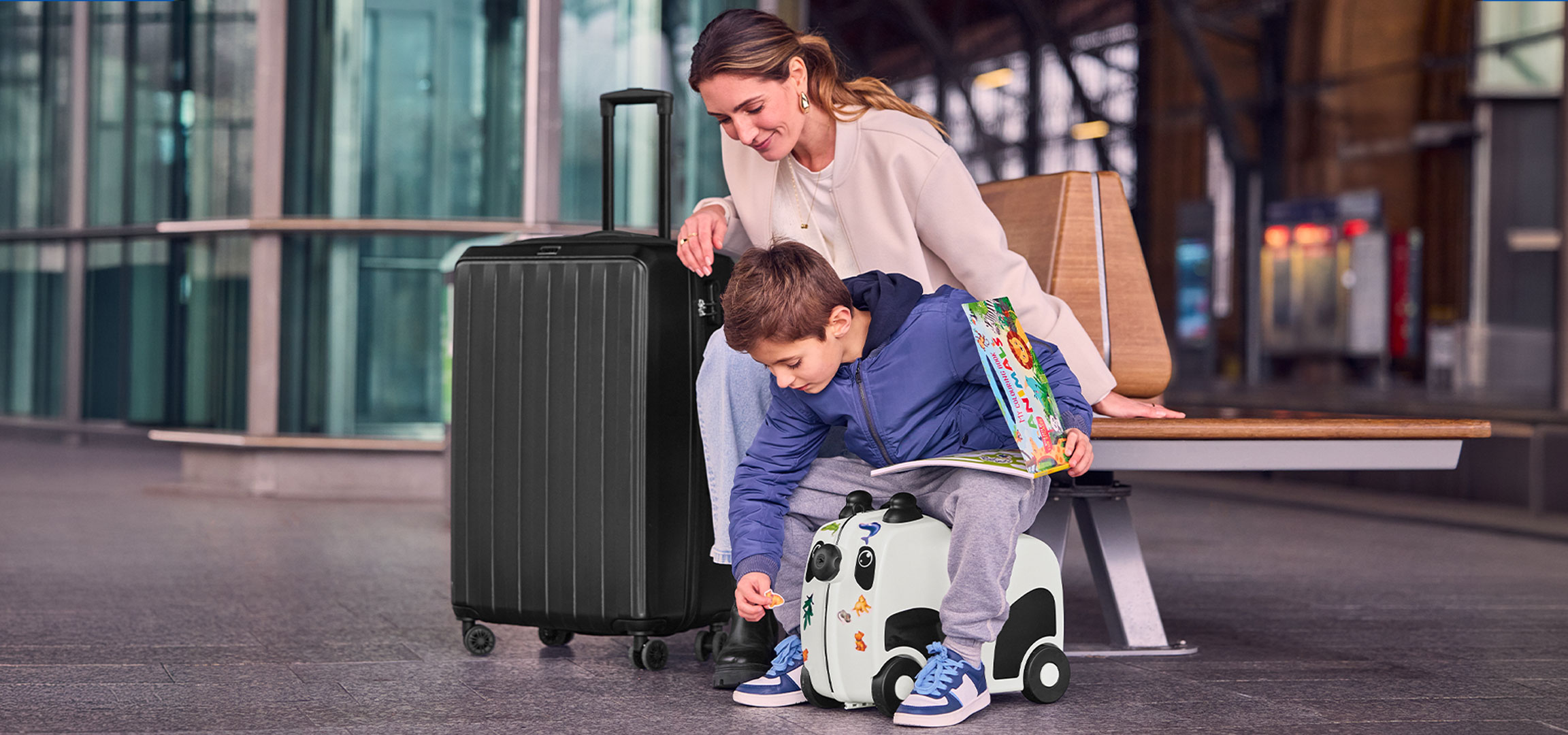 Mutter und Kind mit Gepäck am Flughafen, Kind spielt mit einem Rollkoffer.