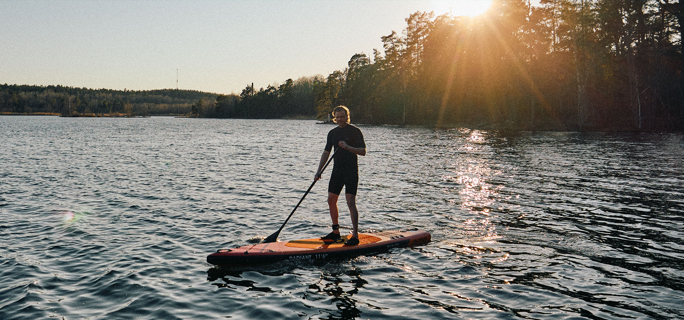 Mann auf einem Stand-Up-Paddleboard auf einem See bei Sonnenuntergang.