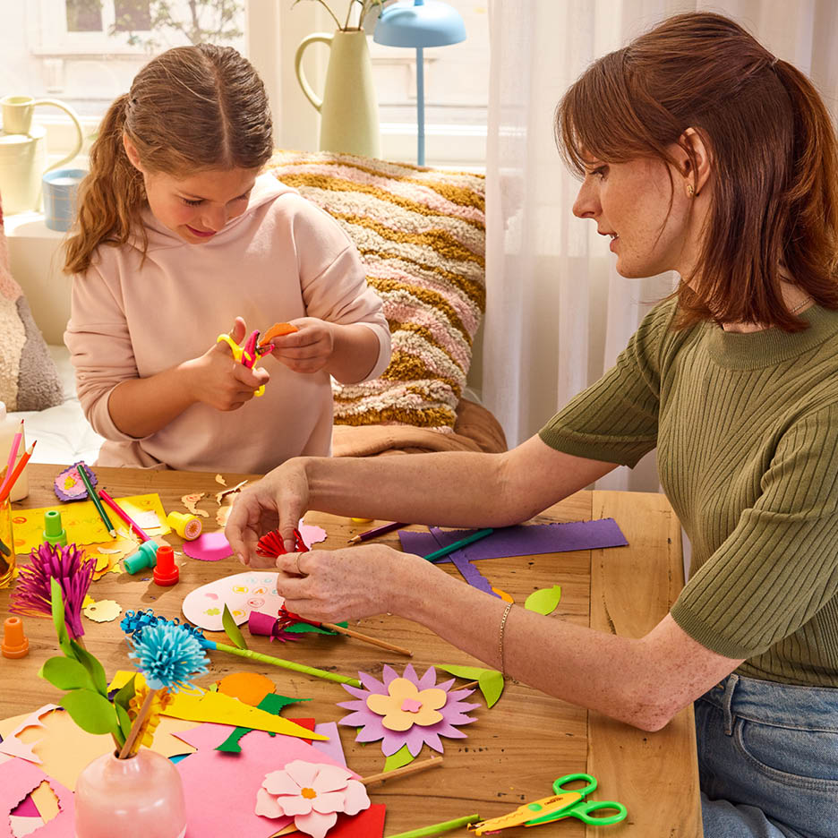 Mutter und Tochter basteln gemeinsam mit Scheren, Buntstiften und Papierblumen.
