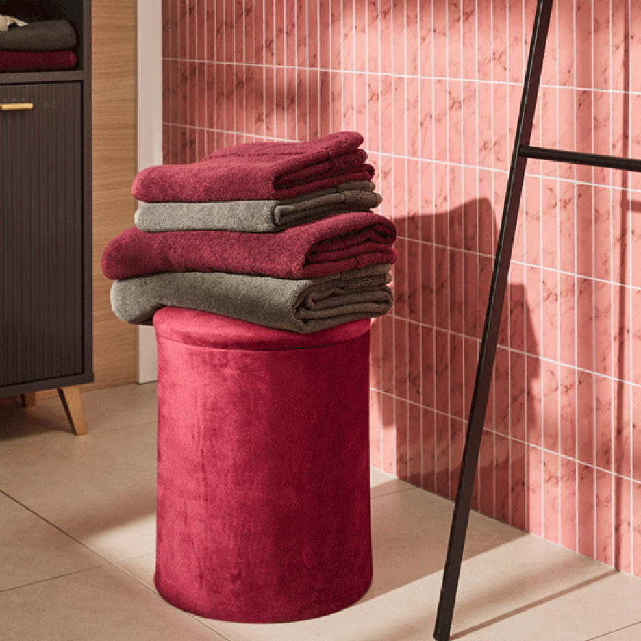 Ein Stapel roter und grauer Handtücher auf einem roten Hocker vor einer rosa gefliesten Wand.