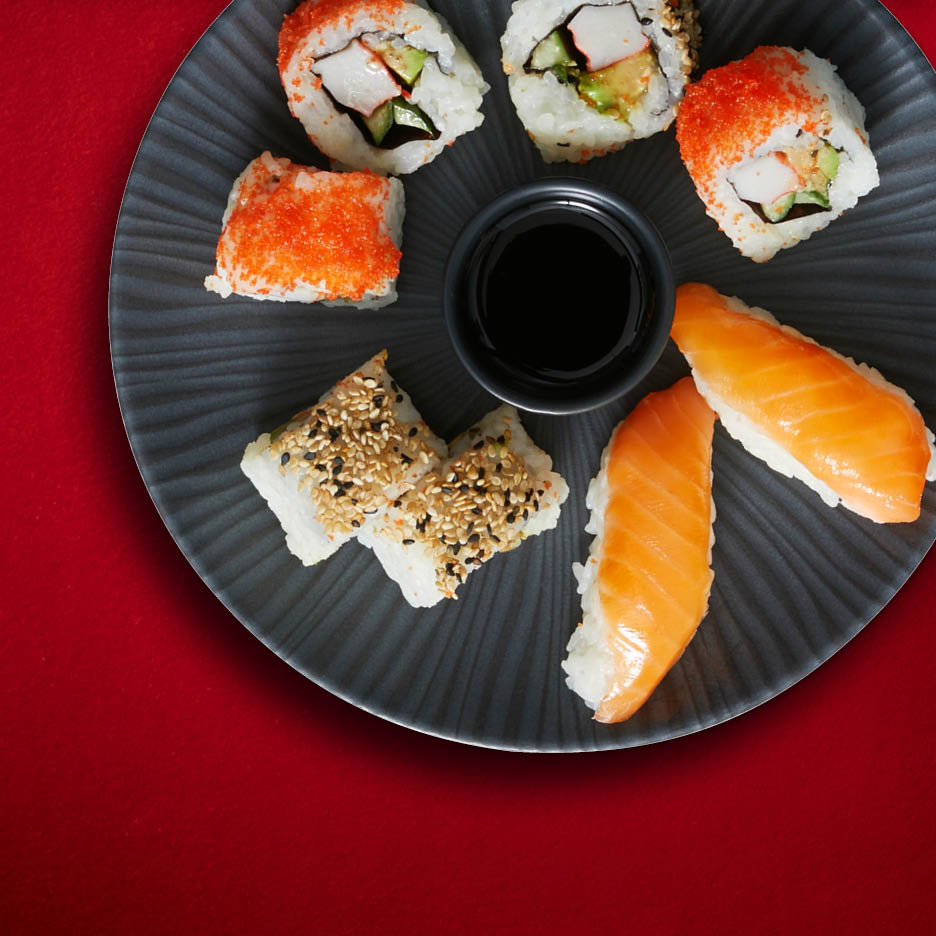 Eine Auswahl an Sushi-Rollen und Nigiri mit Lachs und Sesam auf einem grauen Teller mit Sojasauce.