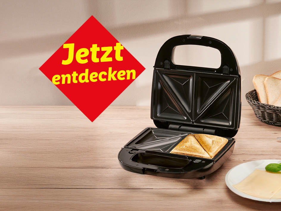 Ein schwarzes Dreiecks-Sandwichtoaster mit getoasteten Brotscheiben darauf, neben einer Scheibe Käse und einem Korb mit Brot.  'Jetzt entdecken' steht auf einem roten Schild.