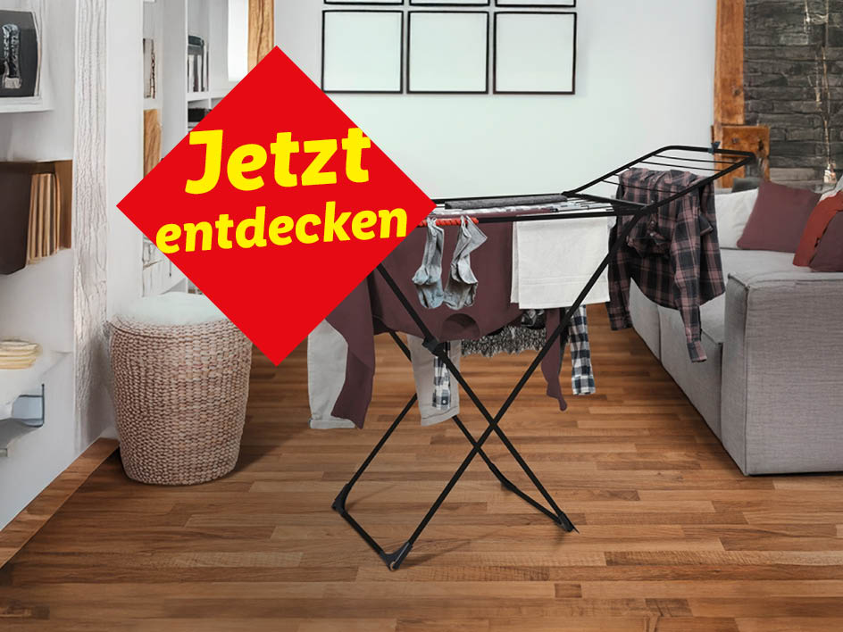 Ein schwarzer Wäscheständer steht in einem Wohnzimmer und ist mit Wäsche behängt.  Ein rotes Schild wirbt mit 'Jetzt entdecken'.