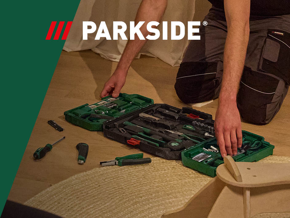 Ein Mann kniet auf dem Boden und sortiert Parkside Werkzeug aus einer grünen Werkzeugbox.