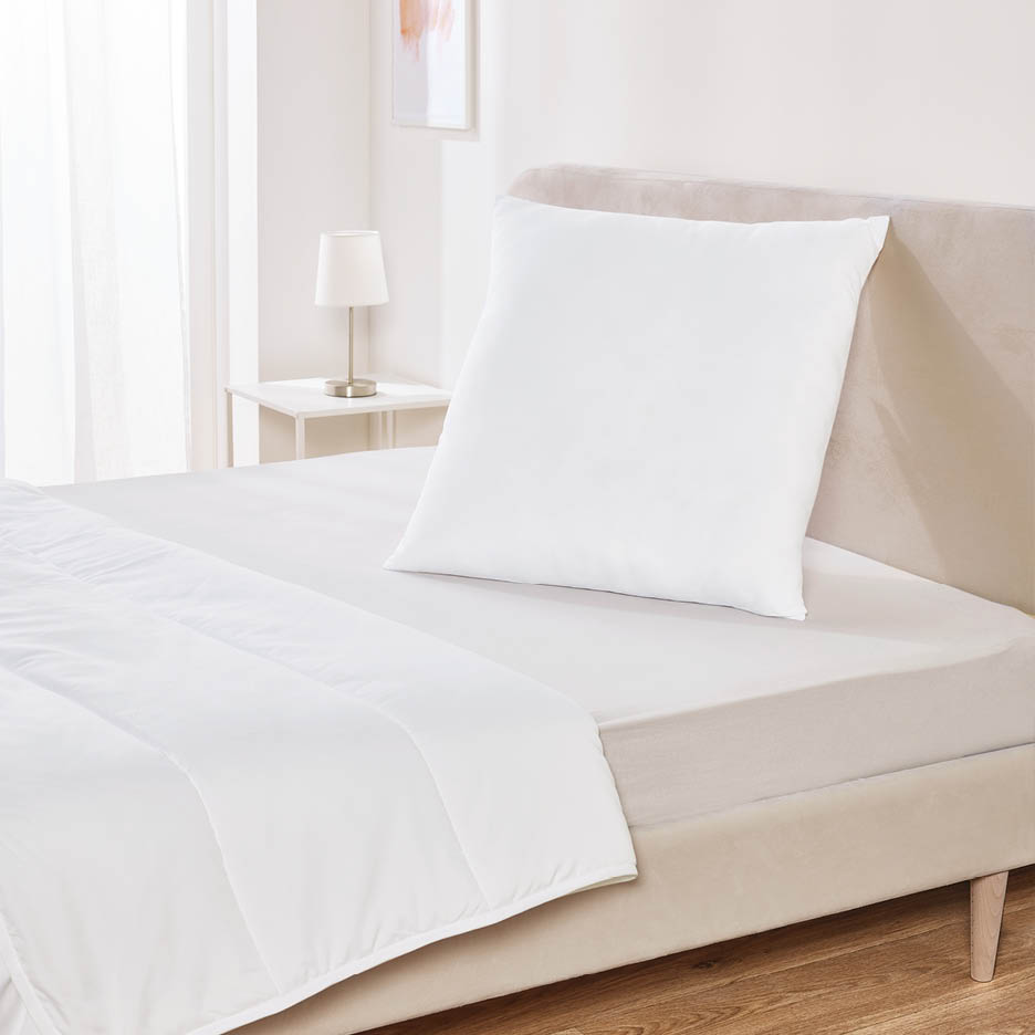 Ein weißes Kissen und eine weiße Bettdecke auf einem Bett in einem hellen Schlafzimmer.