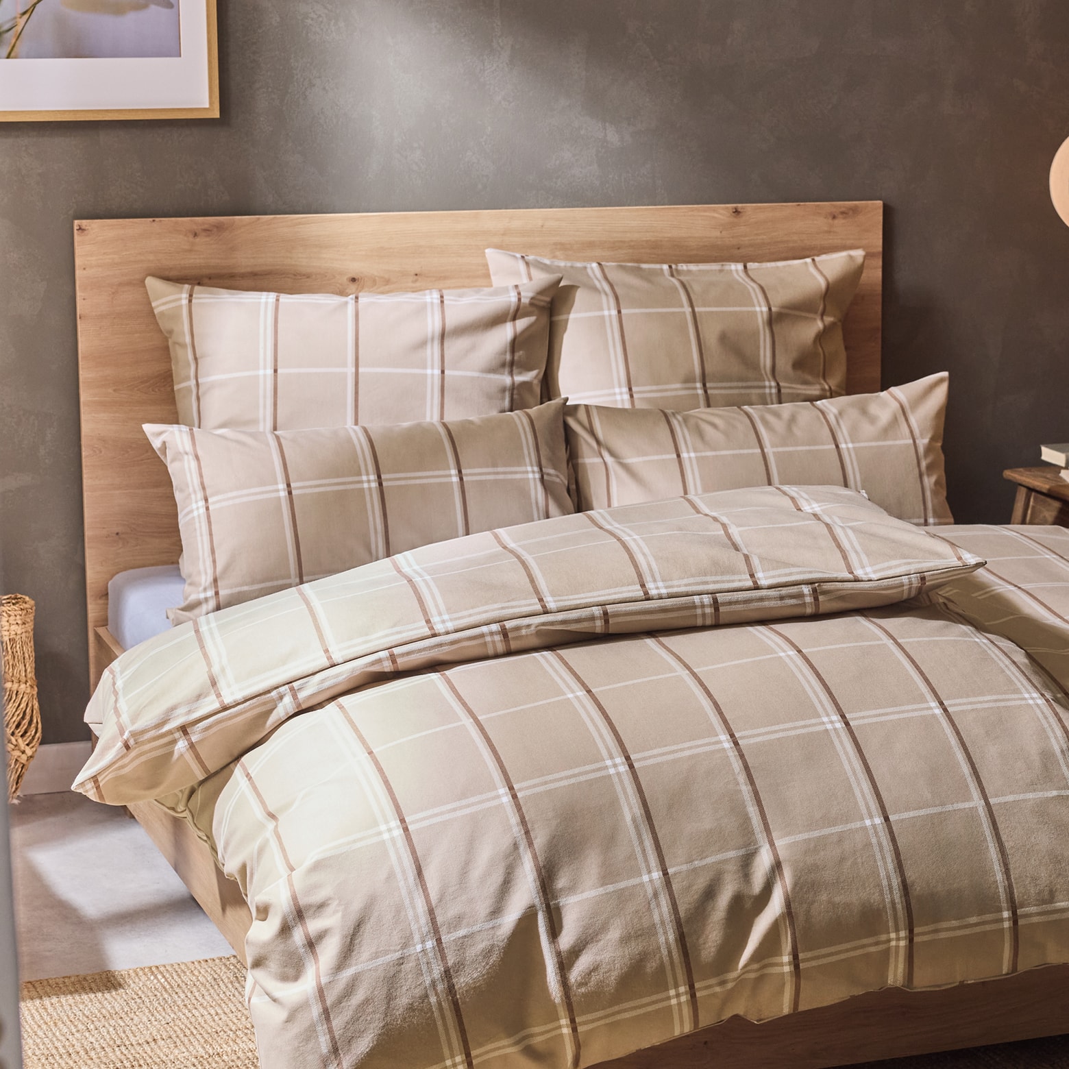 Bett mit beiger Bettwäsche im Karomuster und Holzkopfteil in einem Schlafzimmer.