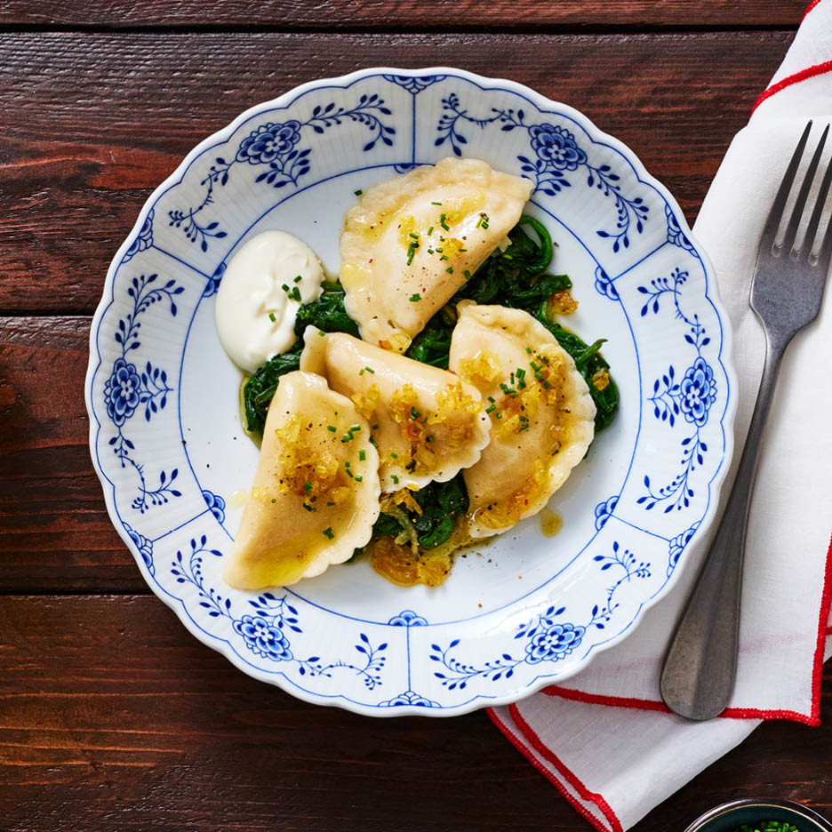Pierogi mit Spinat, Sauerrahm und karamellisierten Zwiebeln auf einem blau-weißen Teller.