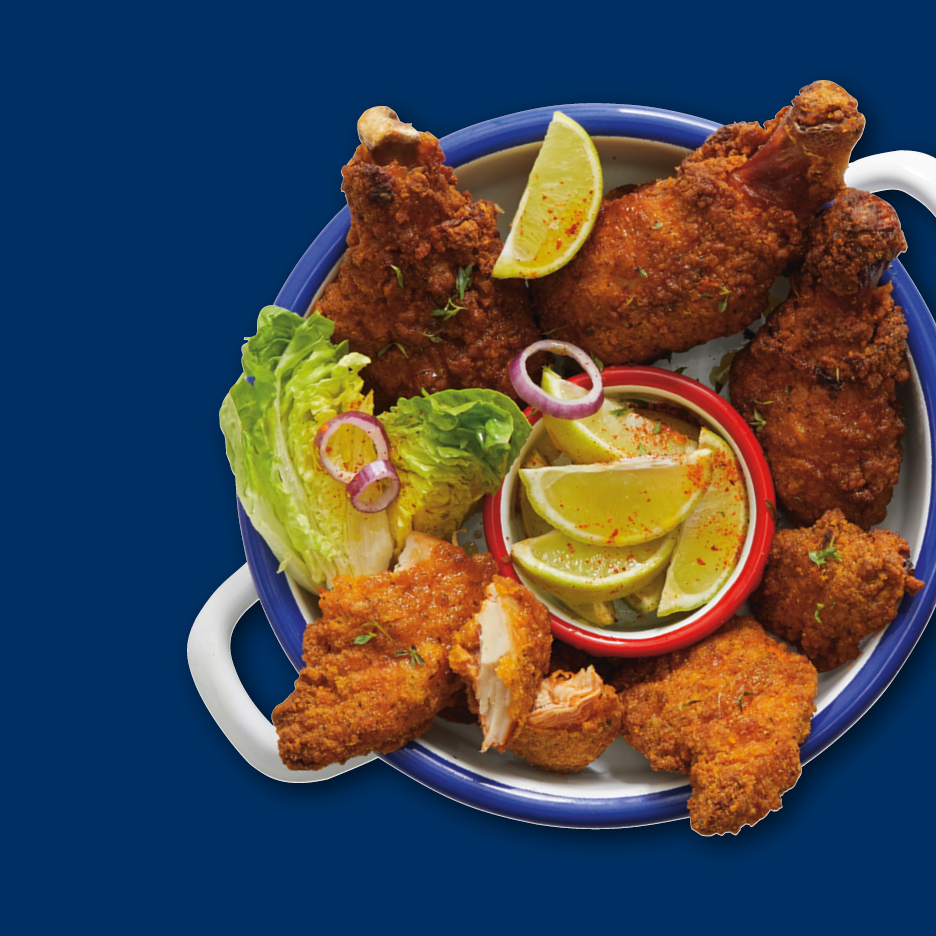 Knusprig gebratenes Hähnchen mit Salat, Zwiebelringen und Limettenspalten in einer Schale.