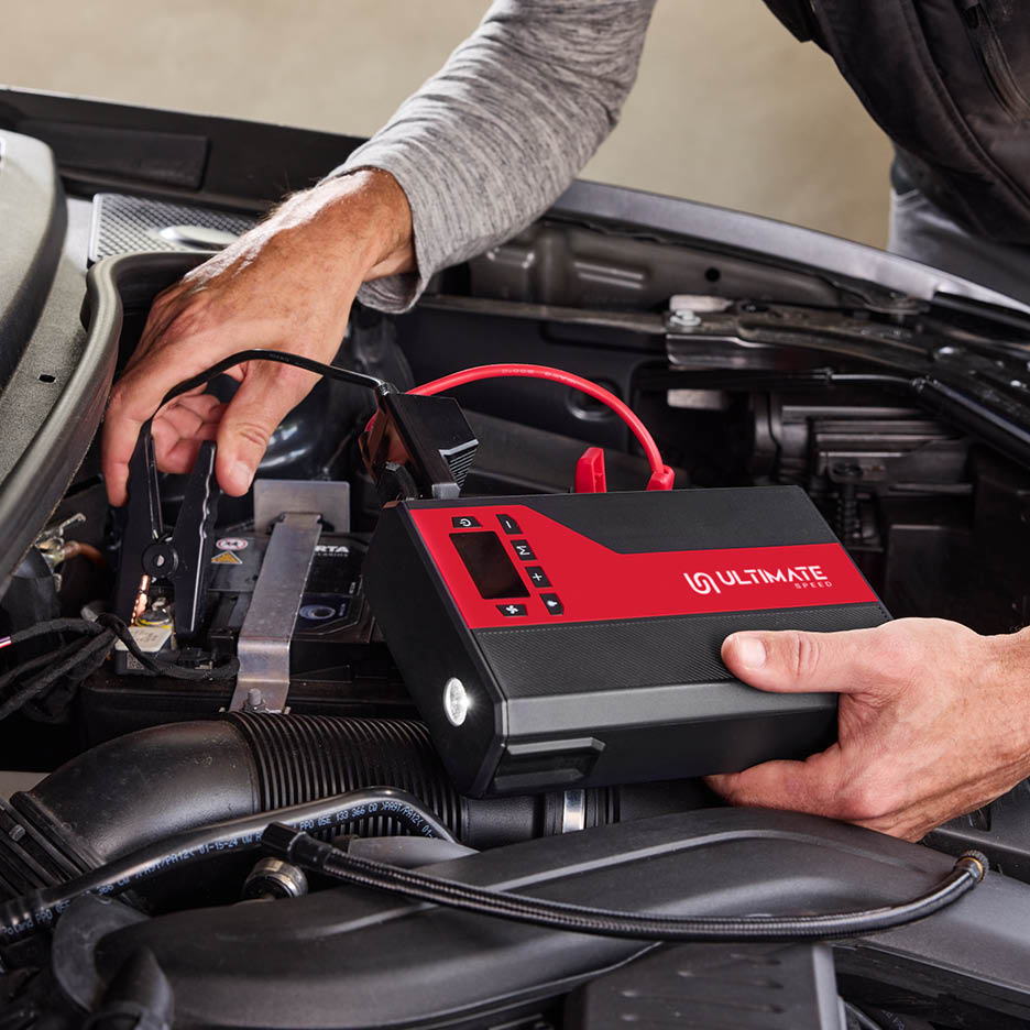 Eine Person schließt ein rotes und schwarzes Starthilfegerät an eine Autobatterie an.