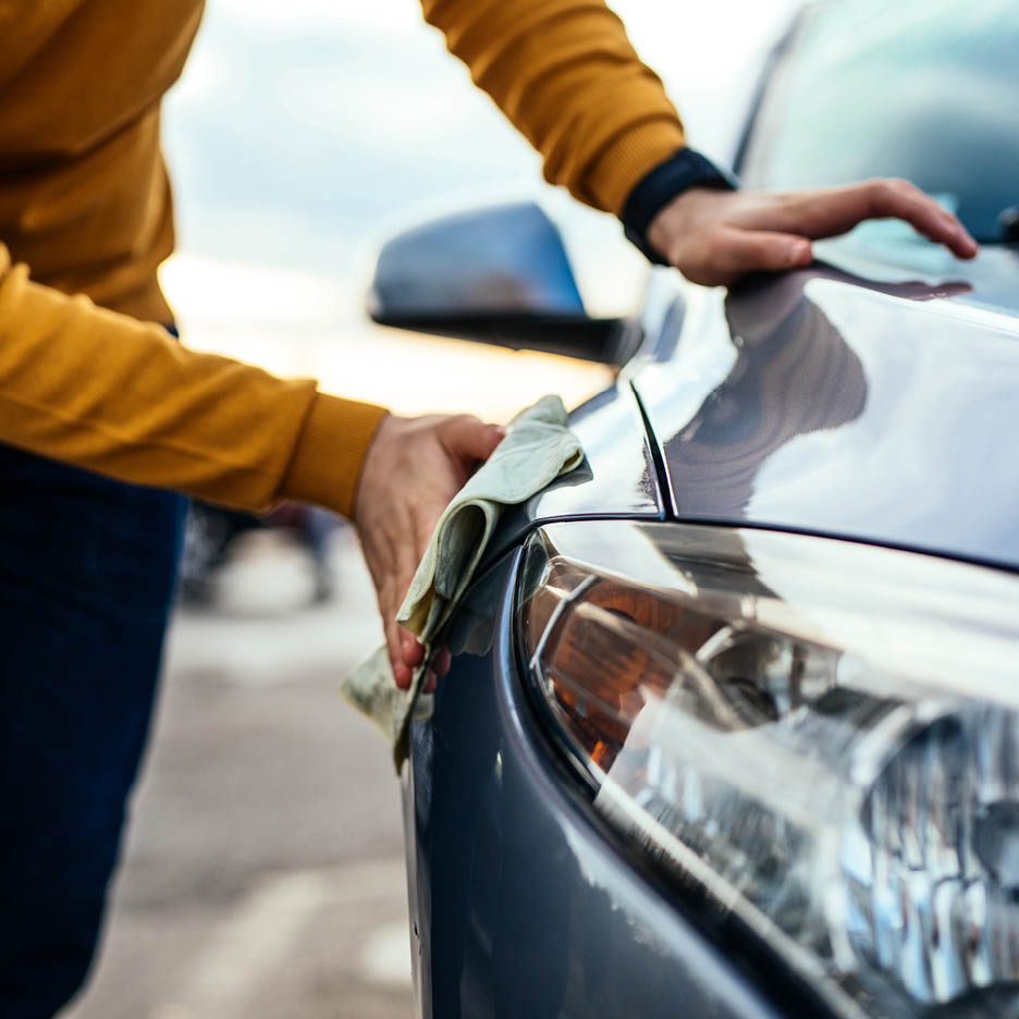 Eine Person poliert die Motorhaube eines Autos mit einem Tuch.