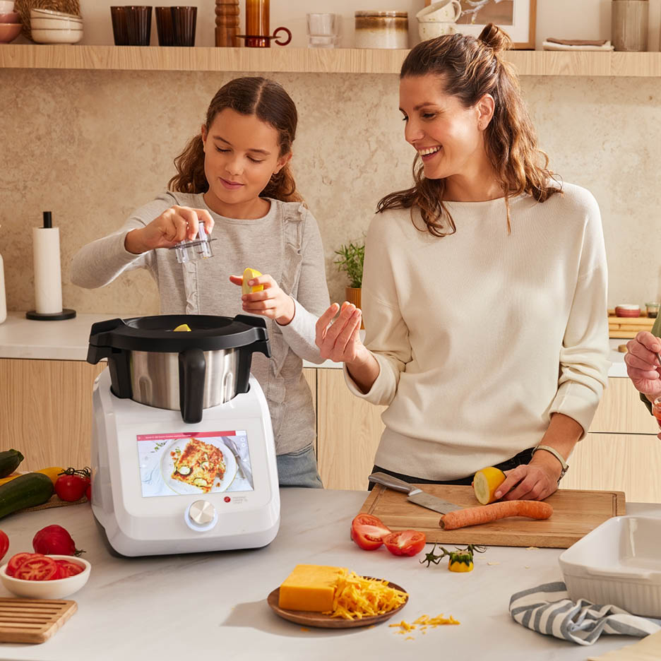 Mutter und Tochter bereiten mit einer Küchenmaschine eine Mahlzeit zu.