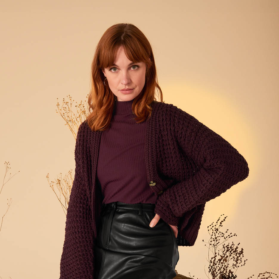 Eine Frau trägt einen weinroten Strickcardigan über einem Rollkragenpullover und einem schwarzen Lederrock.