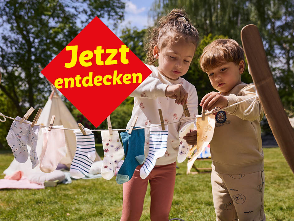 Zwei Kinder hängen Socken und Stoffe an eine Wäscheleine im Garten.