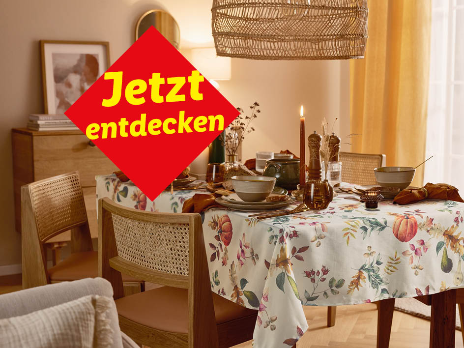 Ein Esstisch mit herbstlicher Tischdecke, Geschirr und Dekoration, mit einem roten Banner „Jetzt entdecken“.