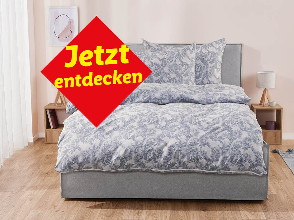 Ein Schlafzimmer mit einem Bett, das mit einer blau-weißen Paisley-Bettwäsche bezogen ist, und dem Text „Jetzt entdecken“.