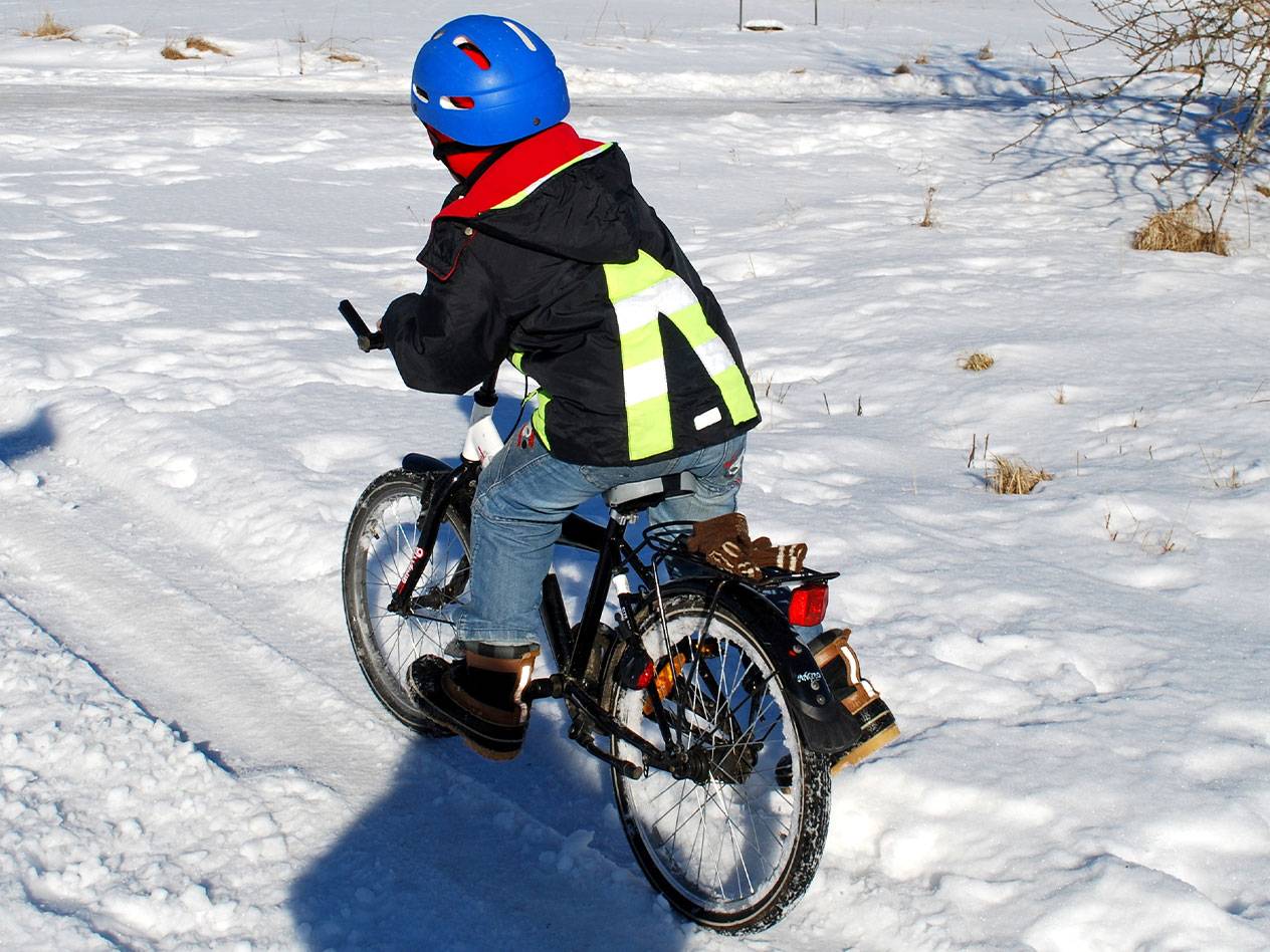 Kind mit blauem Helm und Warnweste fährt Fahrrad im Schnee.