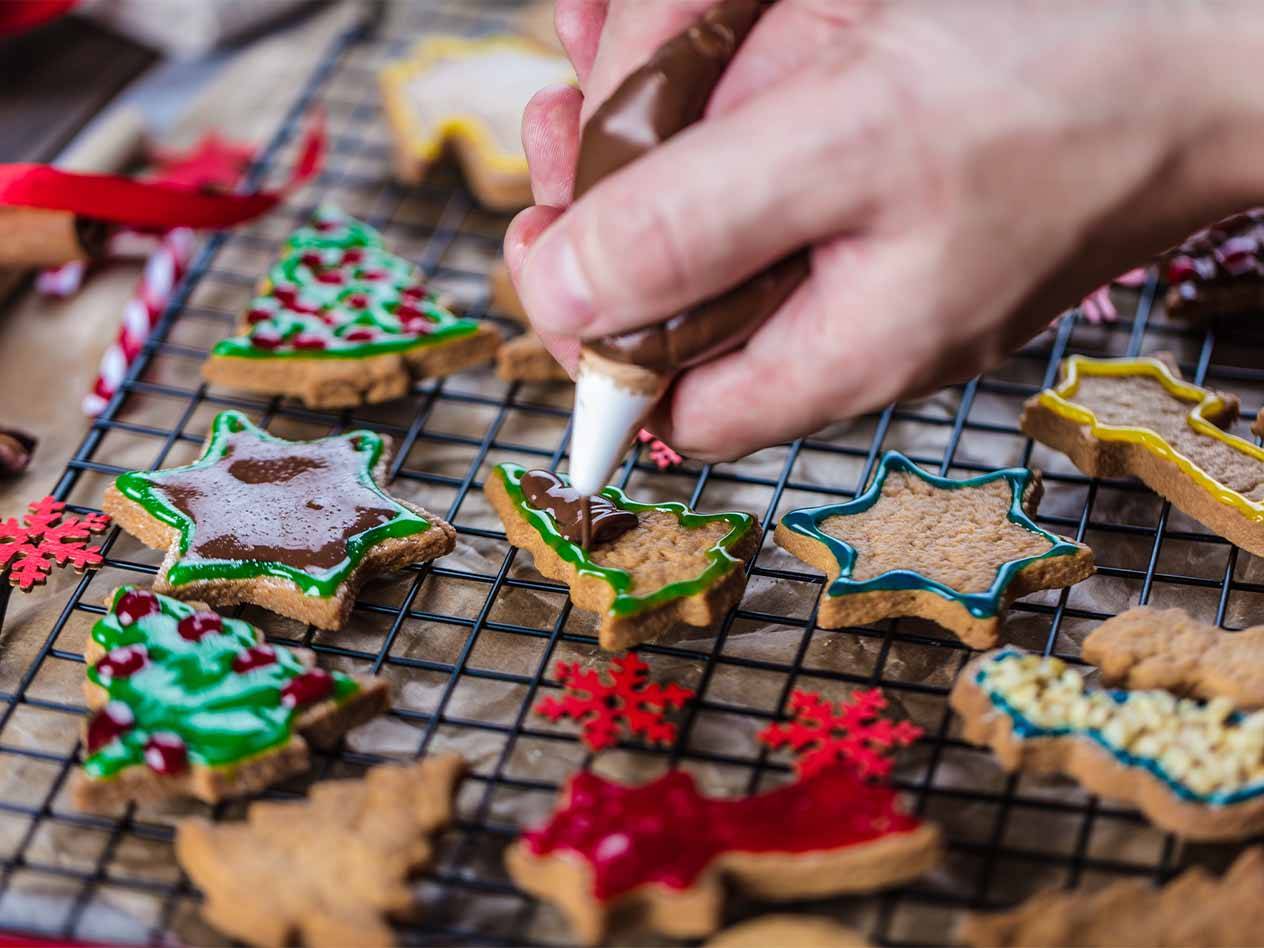 Eine Person verziert Weihnachtsplätzchen in verschiedenen Formen mit Zuckerguss auf einem Drahtgestell.
