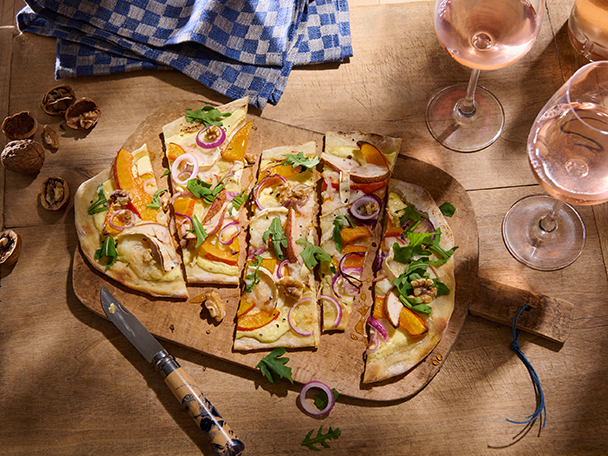Flammkuchen mit Kürbis, Birne, Zwiebeln und Rucola auf Holzbrett mit Roséwein.