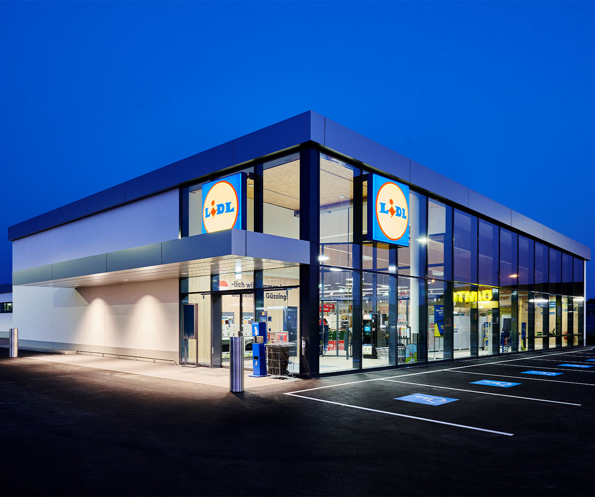 Ein modernes Lidl-Geschäft bei Dämmerung mit beleuchtetem Logo und Parkplätzen.