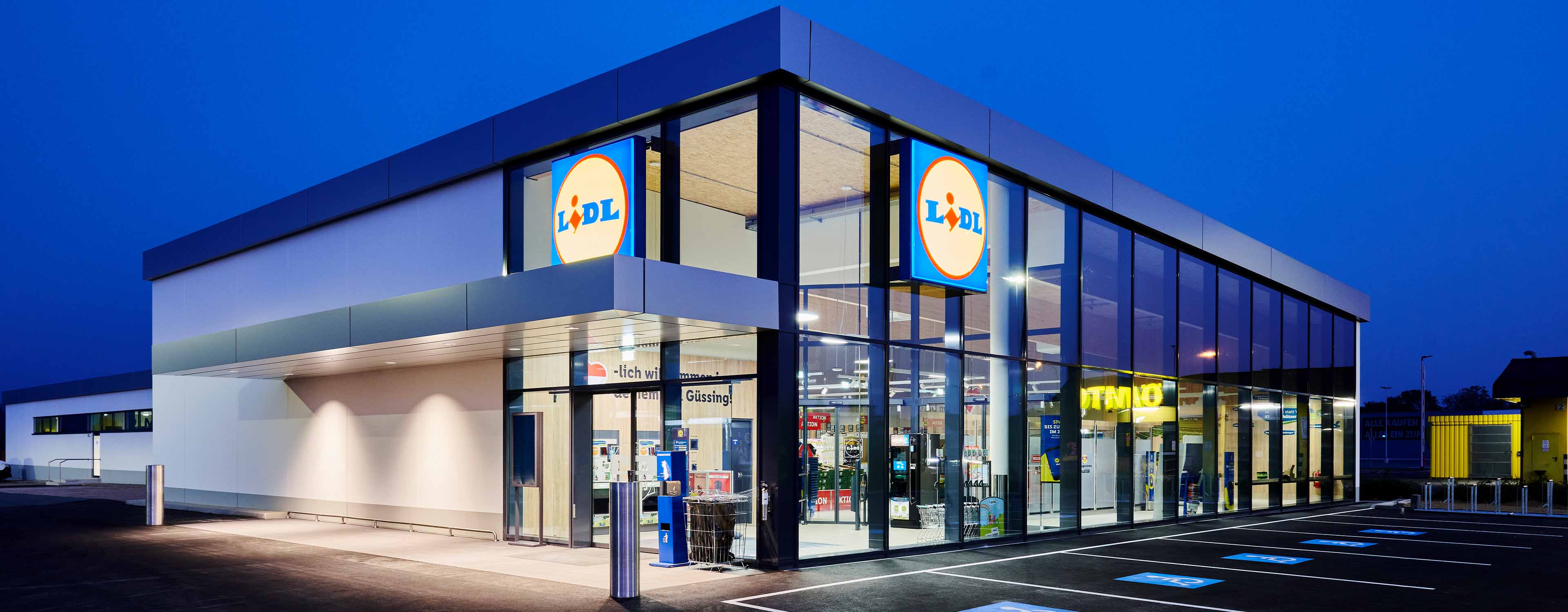 Ein modernes Lidl-Geschäft bei Dämmerung mit beleuchtetem Logo und Parkplätzen.