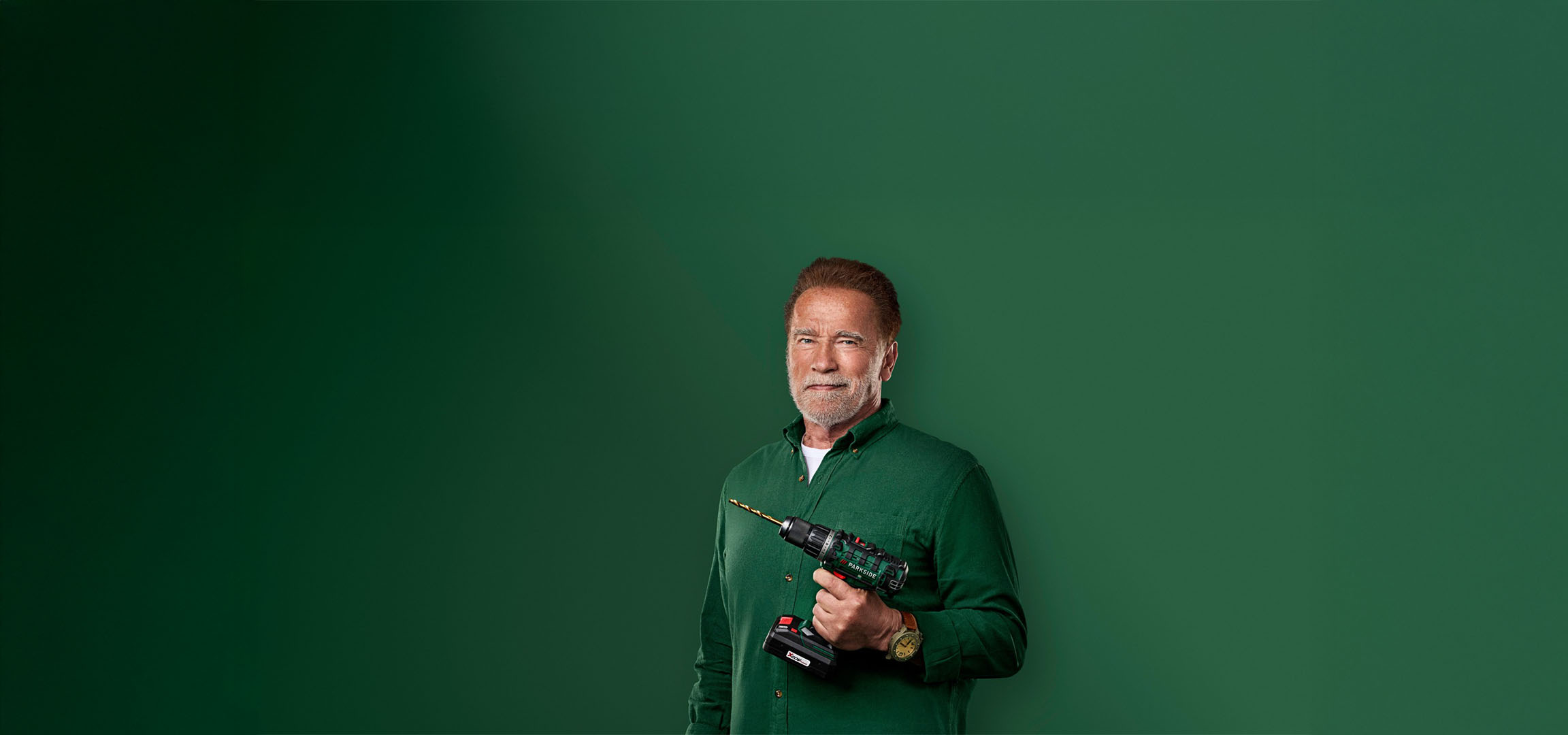 Arnold Schwarzenegger hält einen Parkside Bohrer vor grünem Hintergrund.