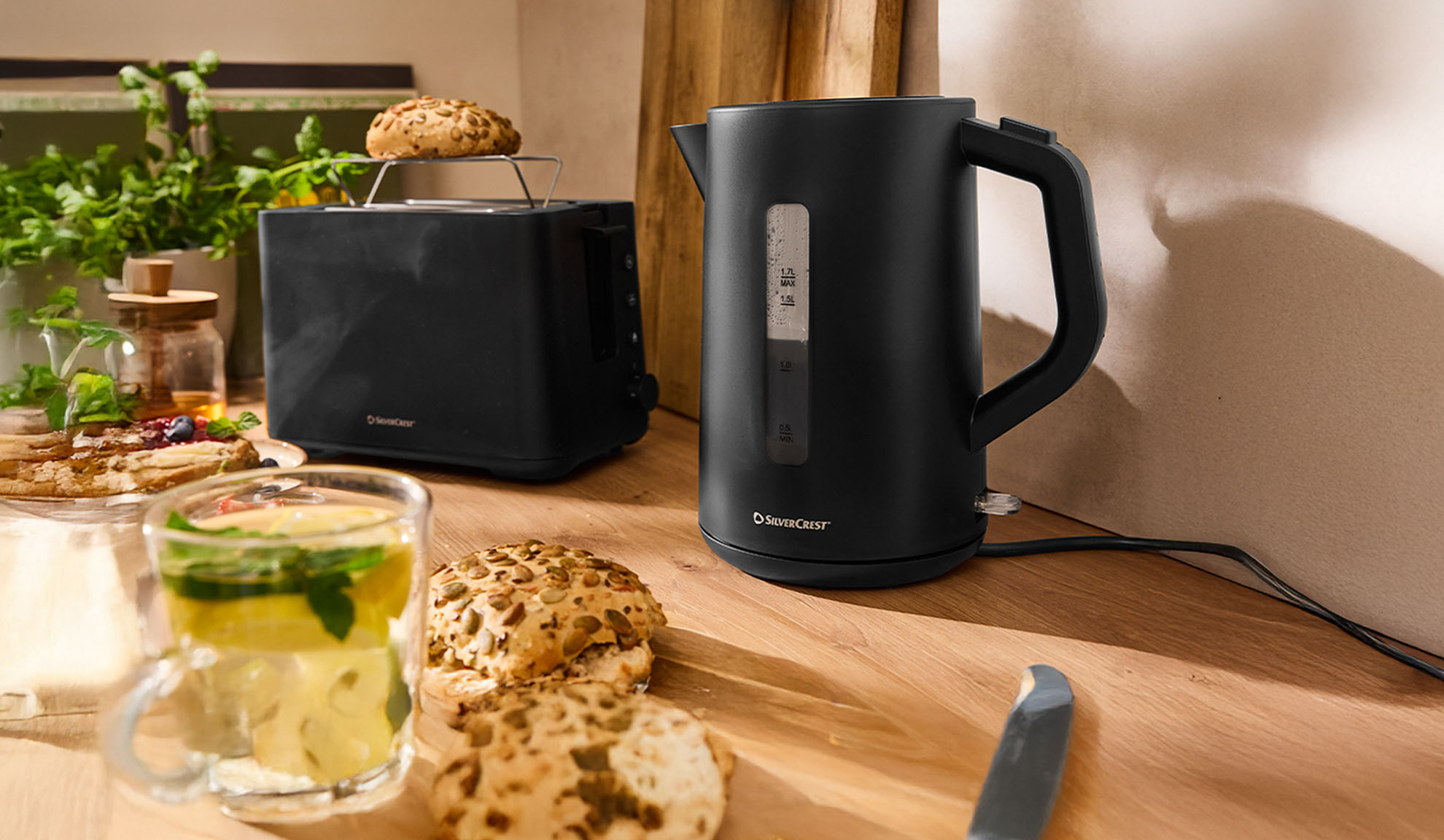 Schwarzer SilverCrest Wasserkocher und Toaster auf einem Holztisch mit Frühstück.