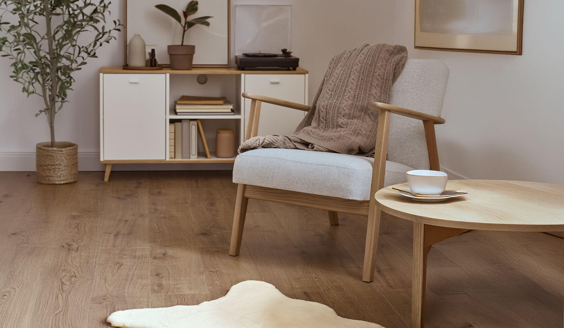 Gemütlicher Sessel mit Decke, Couchtisch aus Holz und Aufbewahrungsschrank in hellem Wohnzimmer.
