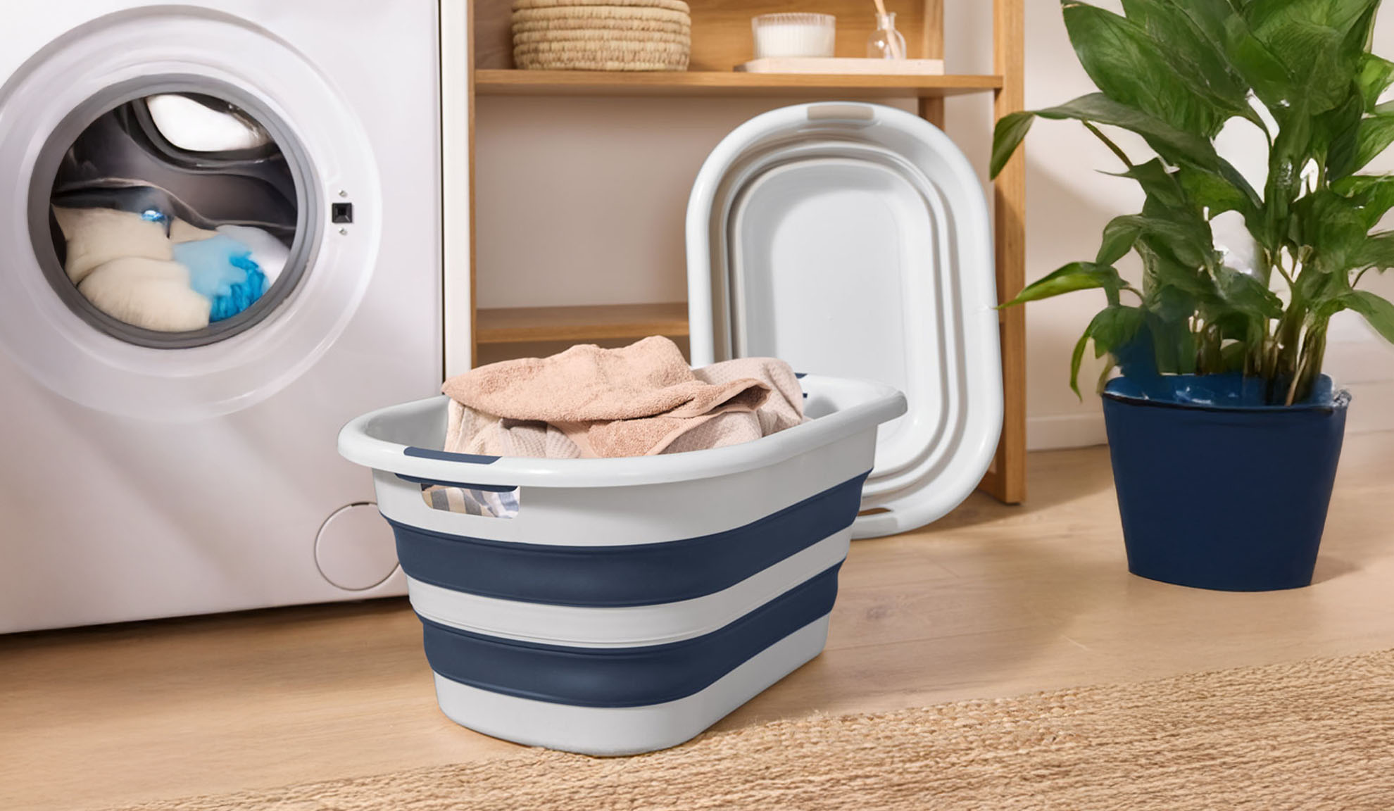 Eine Waschmaschine mit Kleidung, ein faltbarer Wäschekorb und eine Pflanze.