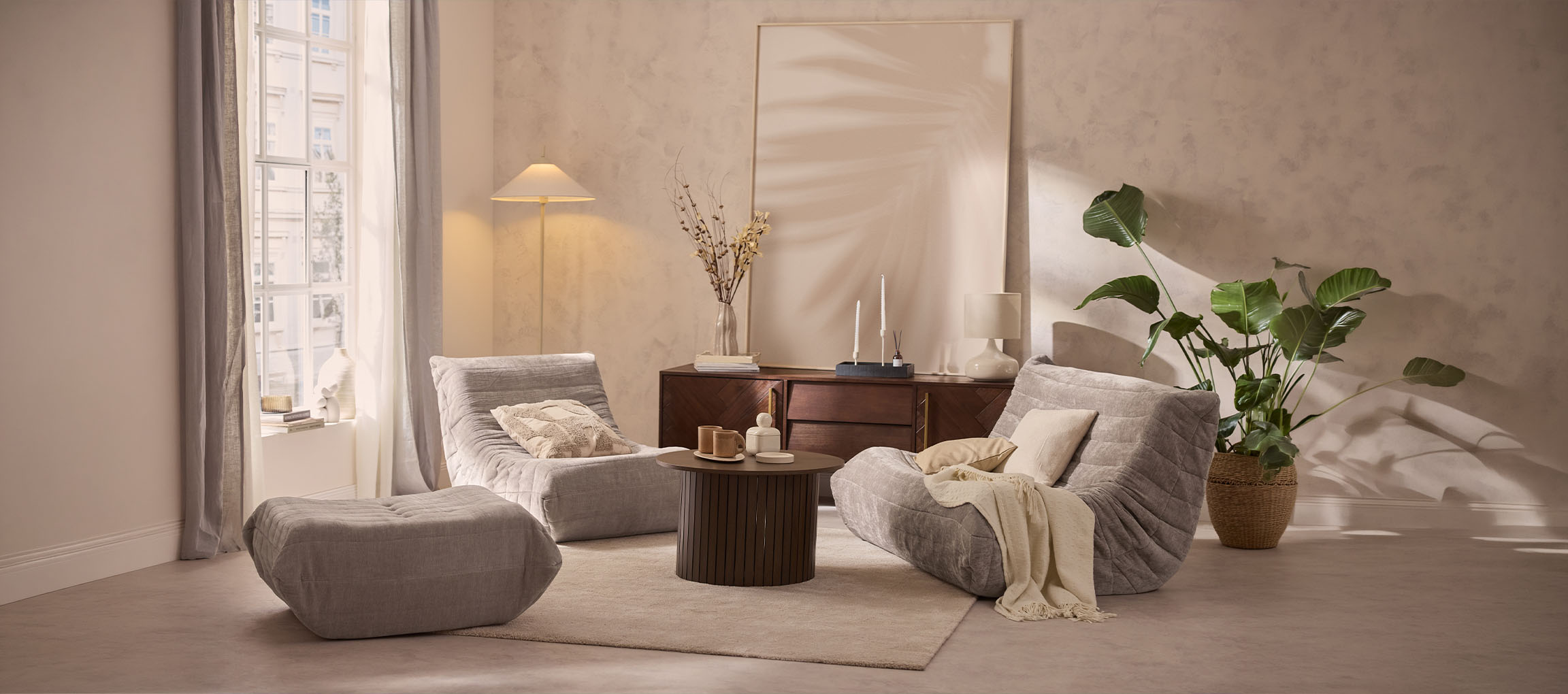 Gemütliches Wohnzimmer mit zwei grauen Loungesesseln, einem Hocker und einem Holztisch.