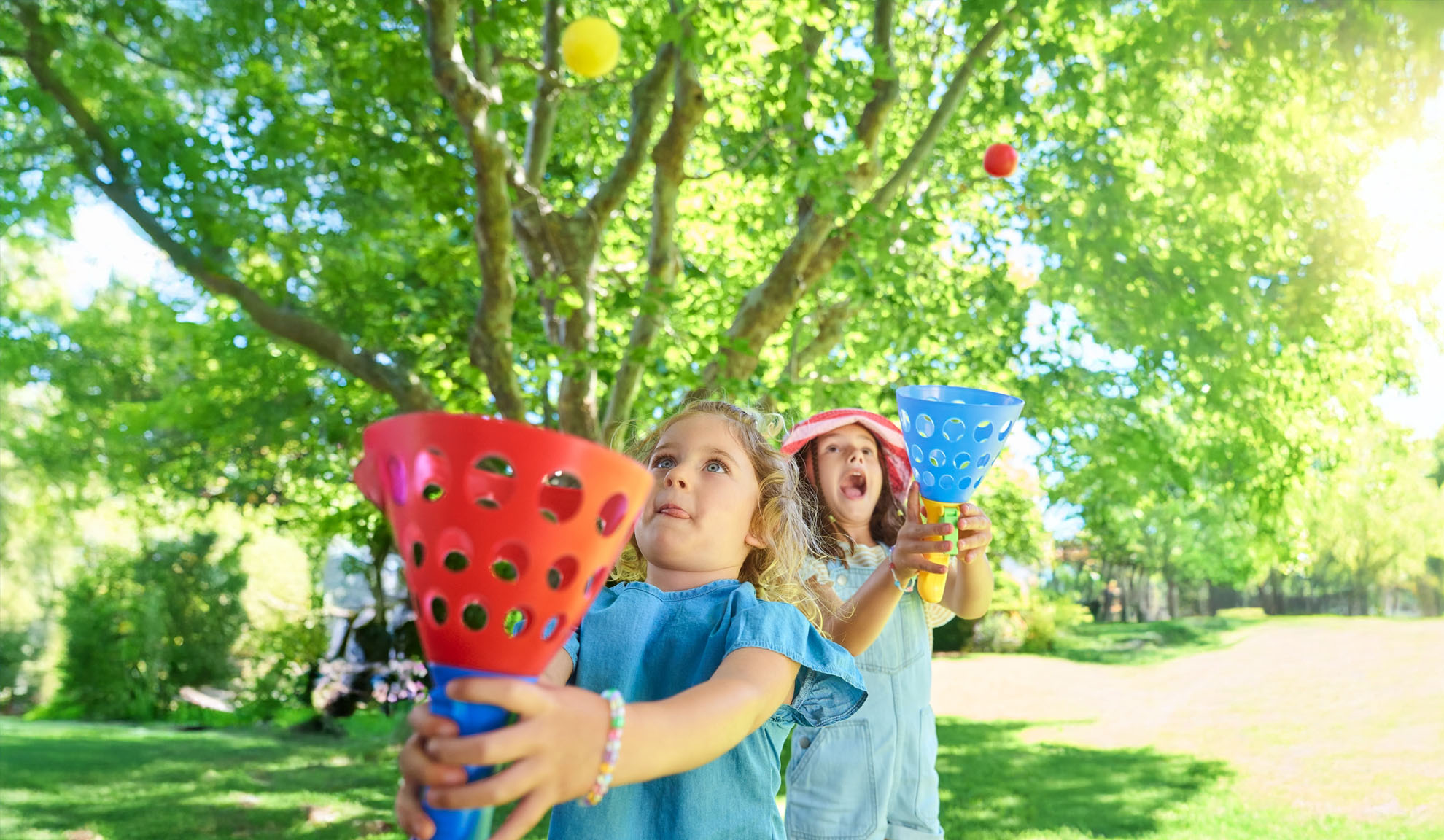 Zwei Mädchen spielen im Freien ein Fangspiel mit bunten Plastikfängern und Bällen.