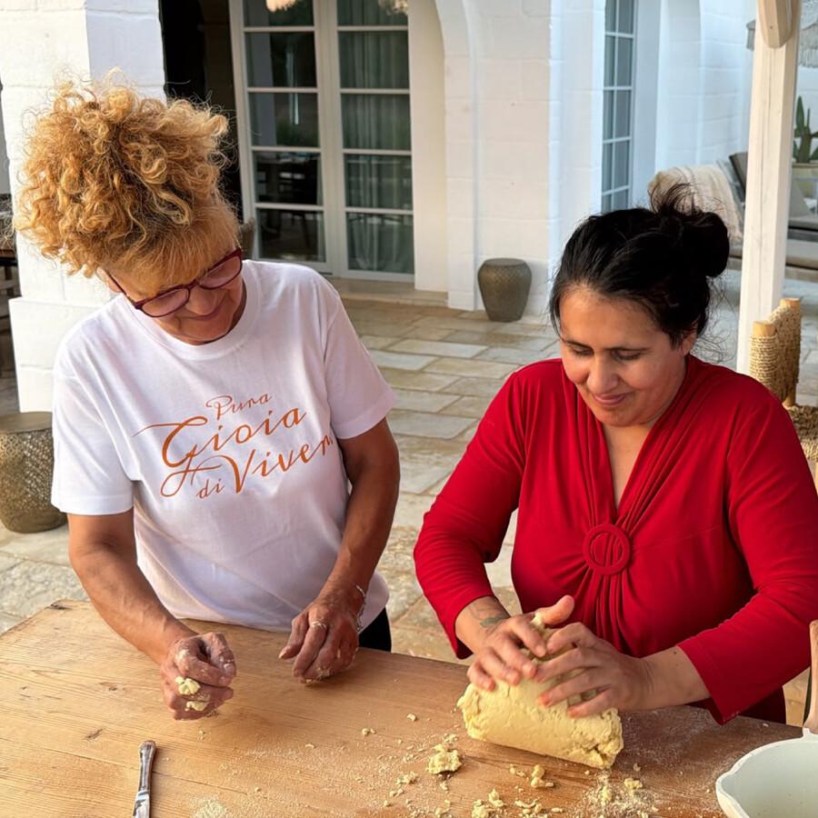 Zwei Frauen kneten Teig auf einem Holztisch.