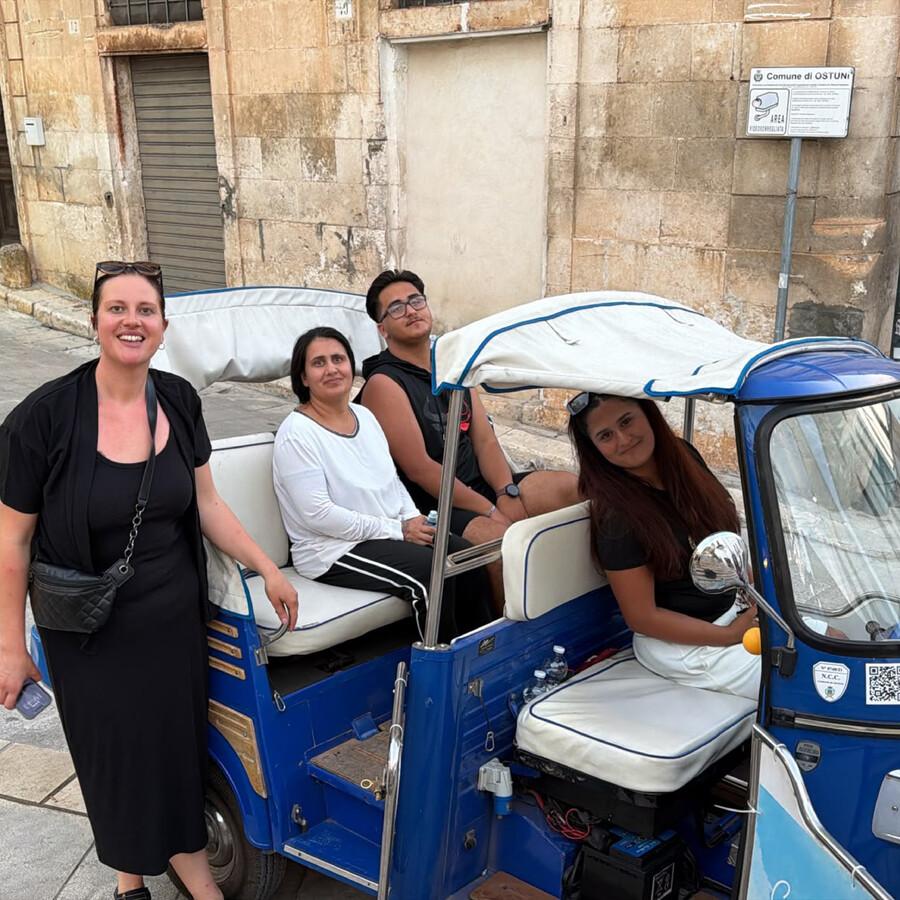 Vier Personen in einem blauen Tuk-Tuk auf einer Straße.