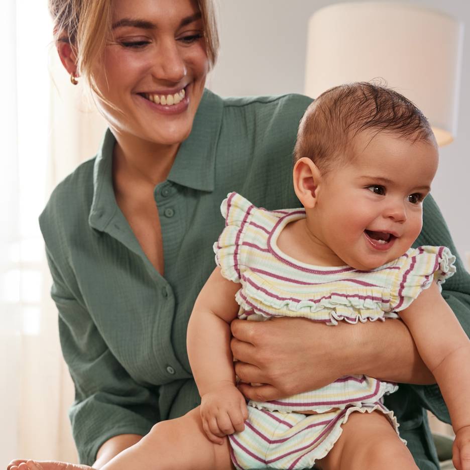 Lächelnde Mutter mit glücklichem Baby in einem bunten gestreiften Outfit.