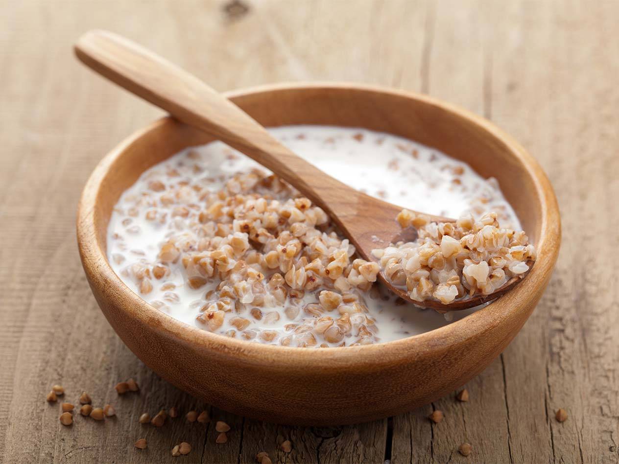 Eine Holzschale mit Buchweizen und Milch, mit einem Holzlöffel darin.
