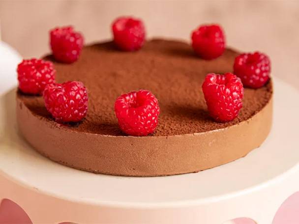 Ein schokoladiger Kuchen mit Himbeeren auf einem rosa Kuchenständer.